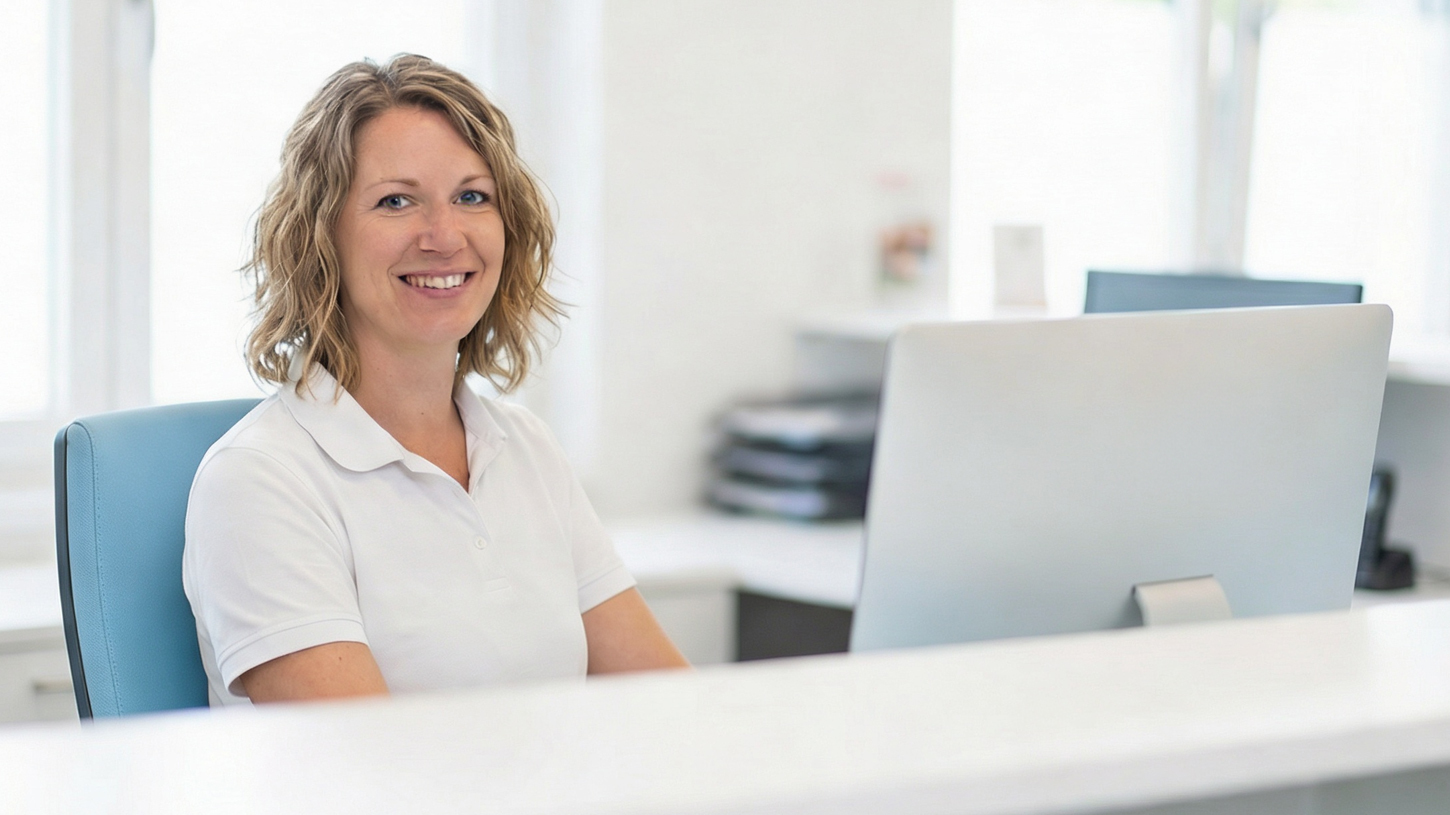 Freundliche Mitarbeiterin Am Empfangstresen Einer Arztpraxis, Die Anfragen Über Das Patientenportal Und Die Online-Rezeption Bearbeitet.